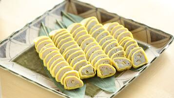 A square plate with neatly arranged yellow and white slices of food, possibly a type of cake or pastry, on a decorative ceramic plate with a geometric pattern.