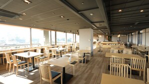 Un comedor amplio con múltiples mesas y sillas, ventanas grandes que ofrecen vistas de la ciudad y un diseño de techo moderno.