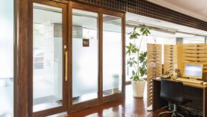 Un área de recepción con un escritorio de madera, computadora y una planta en maceta.