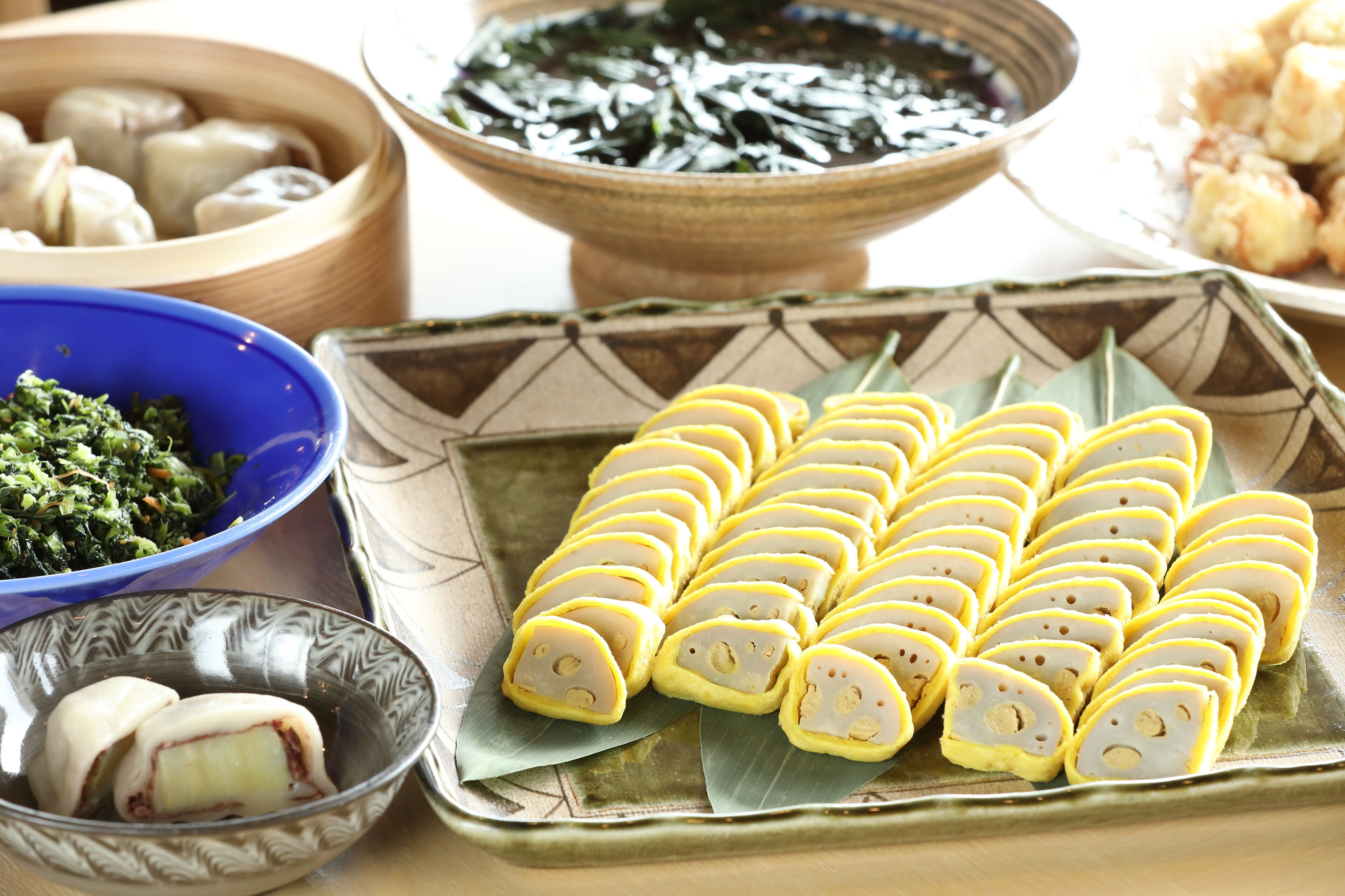A variety of dishes including dumplings, a bowl of greens, and a plate of sliced rolls.