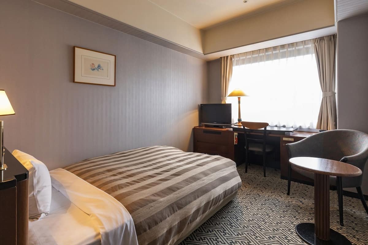 A hotel room with a bed, a desk with a computer, a chair, and a television.