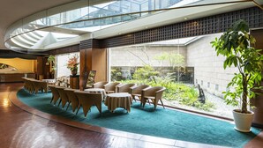 Un vestíbulo amplio con techo curvo, una zona de estar con sillones de mimbre, una mesa redonda y vistas a un jardín a través de amplias ventanas.