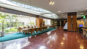 Un vestíbulo amplio con techo curvo, una recepción y una zona de estar con mobiliario de mimbre.
