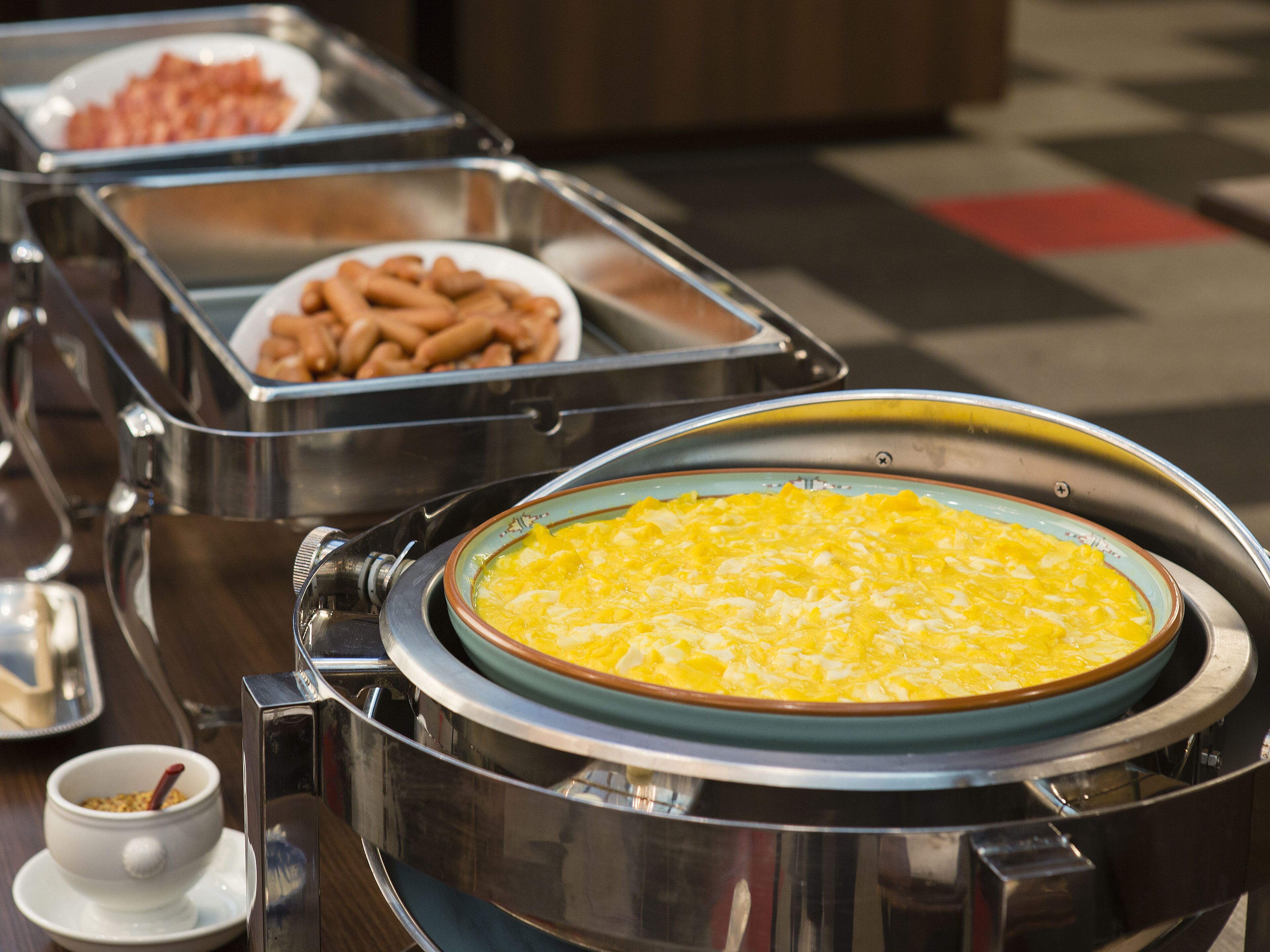 Ein reichhaltiges Buffet mit verschiedenen Speisen, darunter Rührei, Würstchen und eine Schüssel Müsli.