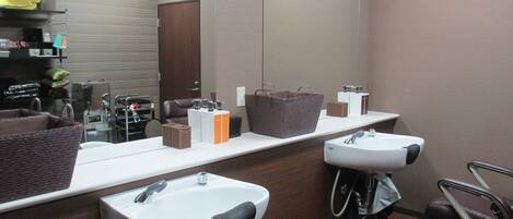 A bathroom with two sinks, a mirror, a clock, and a seating area.