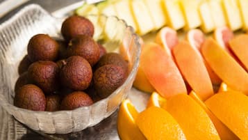 A clear glass bowl filled with round, brown fruits, and sliced orange segments on a metal tray.