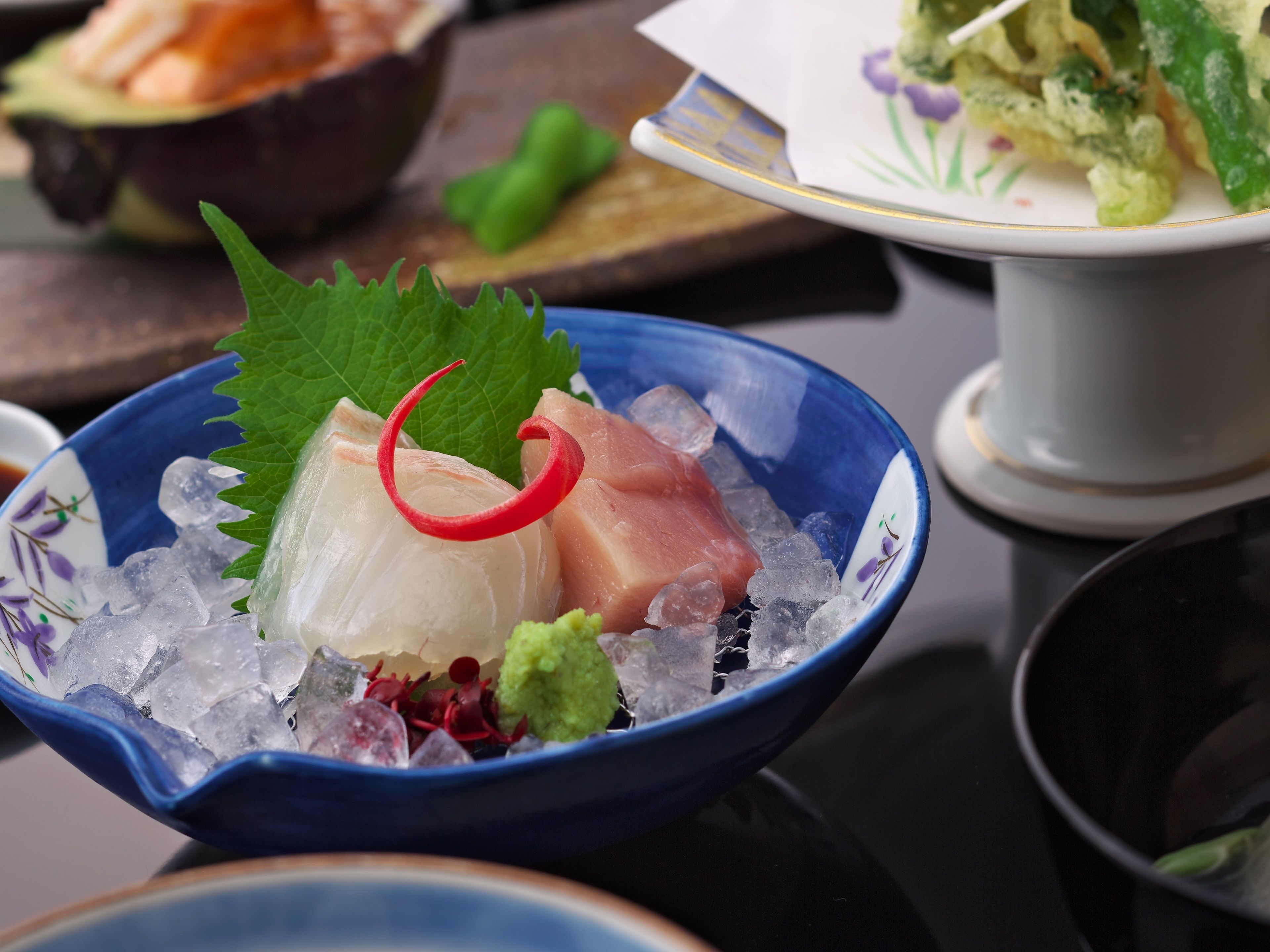 Un bol de sashimi servi sur de la glace, agrémenté d’une feuille et d’un piment rouge.