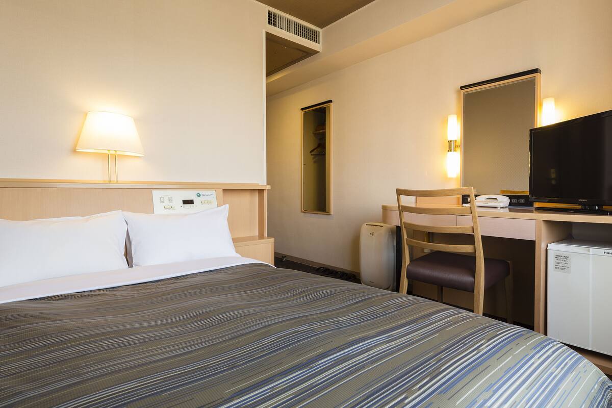 Une chambre d’hôtel équipée d’un lit, d’un bureau, d’une chaise, d’une télévision et d’un mini-bar.