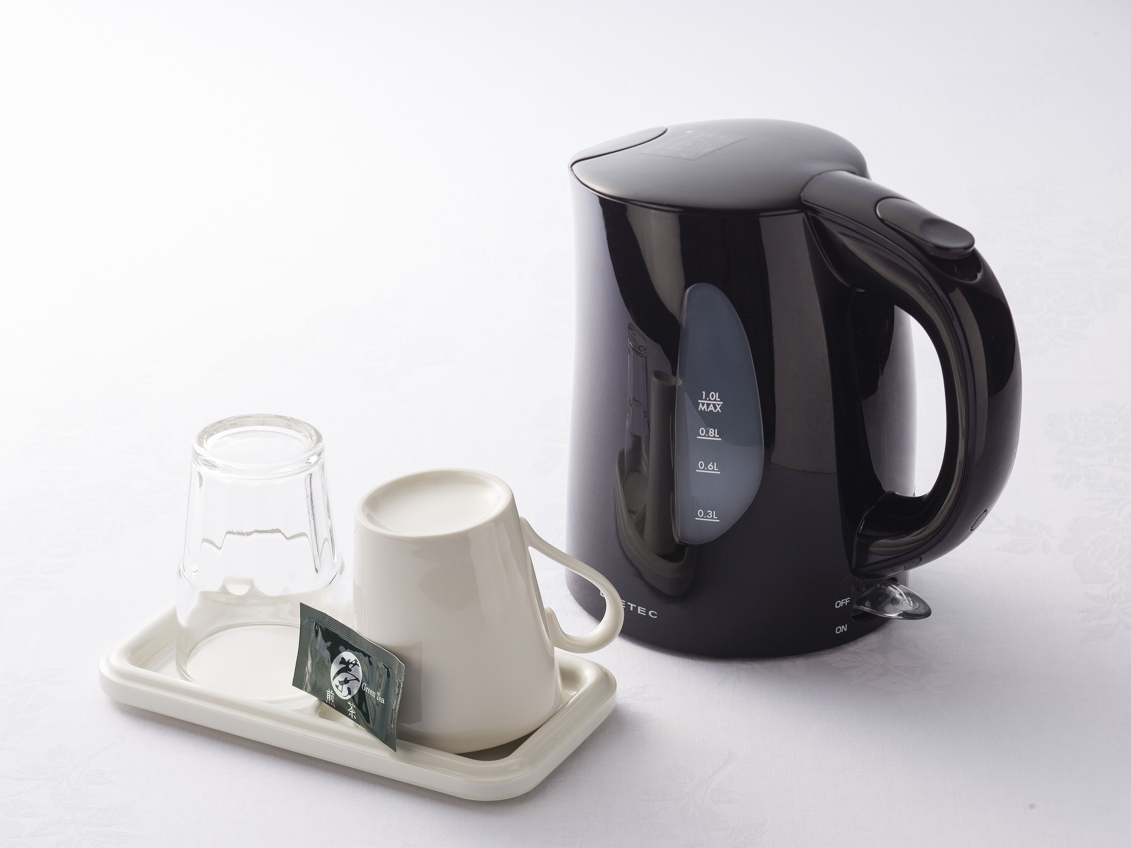 Un bollitore elettrico nero, una tazza bianca e un bicchiere su un vassoio con una bustina di tè.