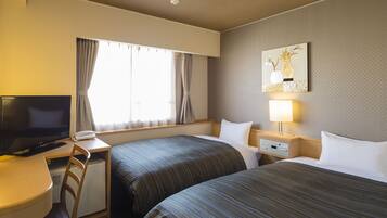 A hotel room with two beds, a desk with a TV, a chair, a bedside table with a lamp, and a window with curtains.