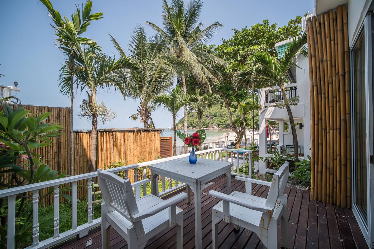 A wooden deck with white furniture and a vase of red flowers.