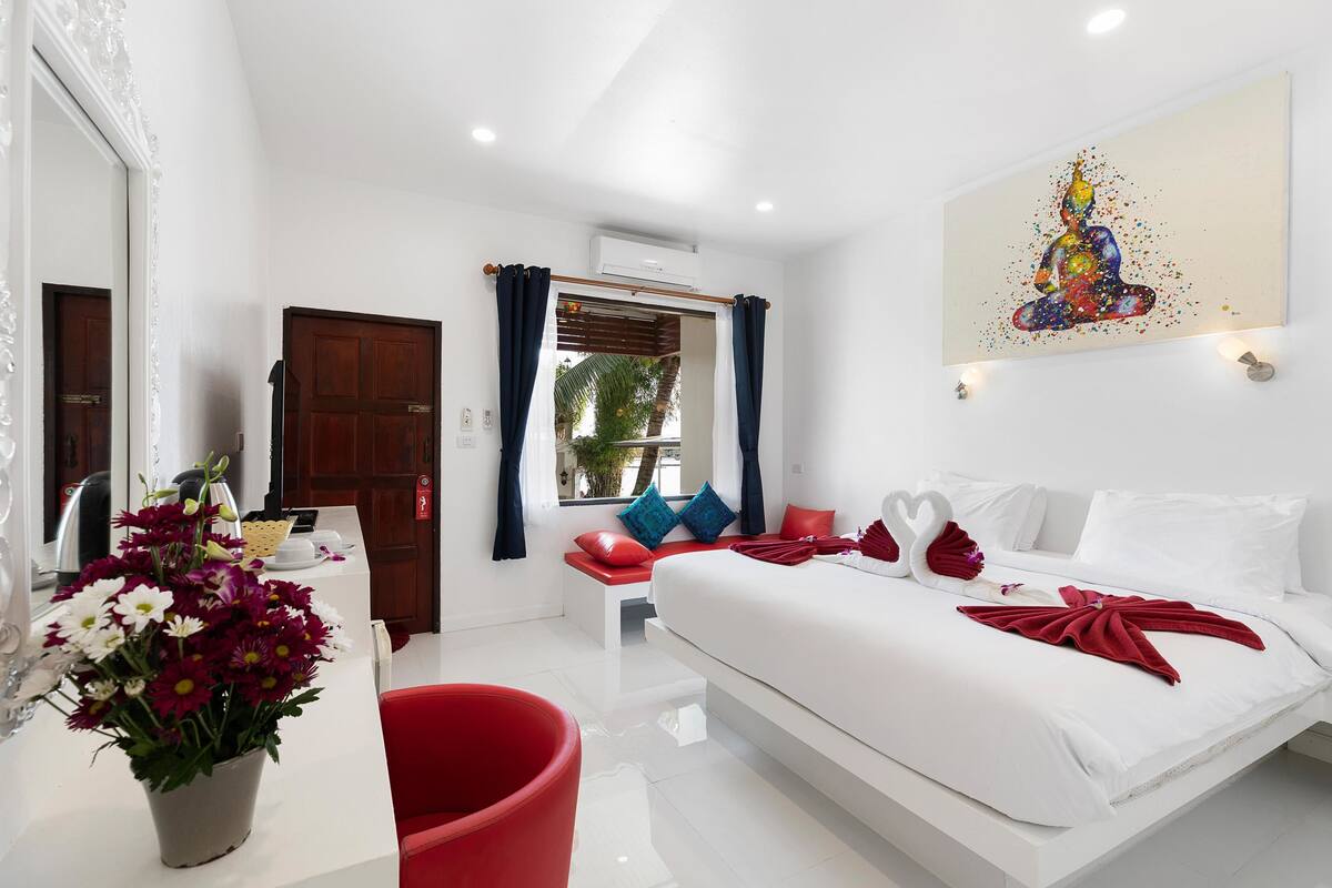 A modern hotel room with a large bed, a desk with a vase of flowers, and a view of the outdoors.