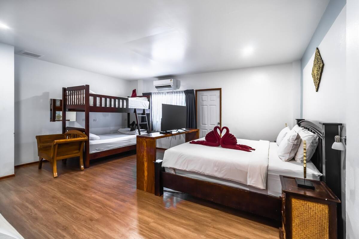 A hotel room with bunk beds, a desk, a television, and a bed with a red towel.