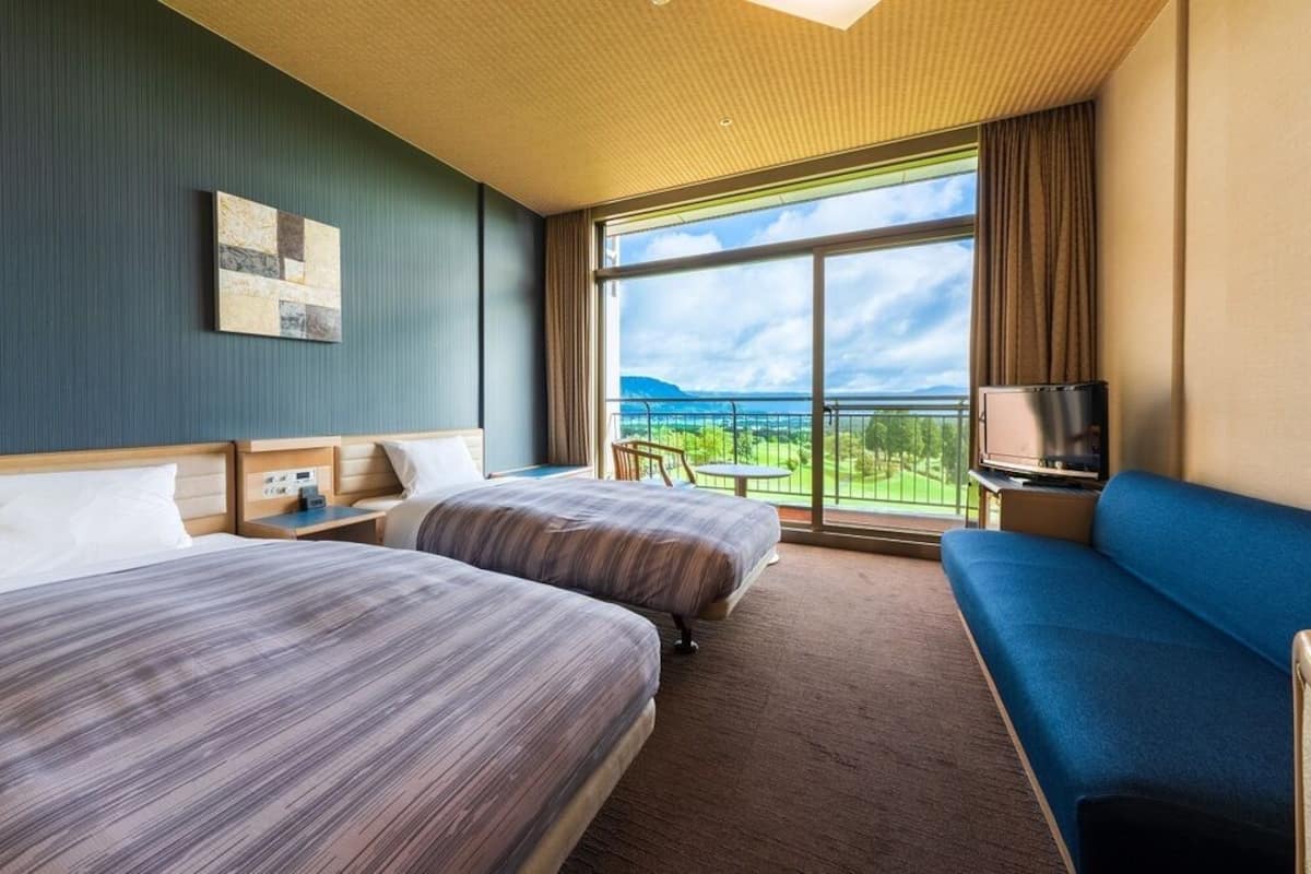 A hotel room with two beds, a sofa, a TV, and a balcony with a view.