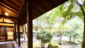 A covered walkway with a view of a garden area, including a small tree and moss-covered ground. - Aso Resort Grandvrio Hotel (Aso)