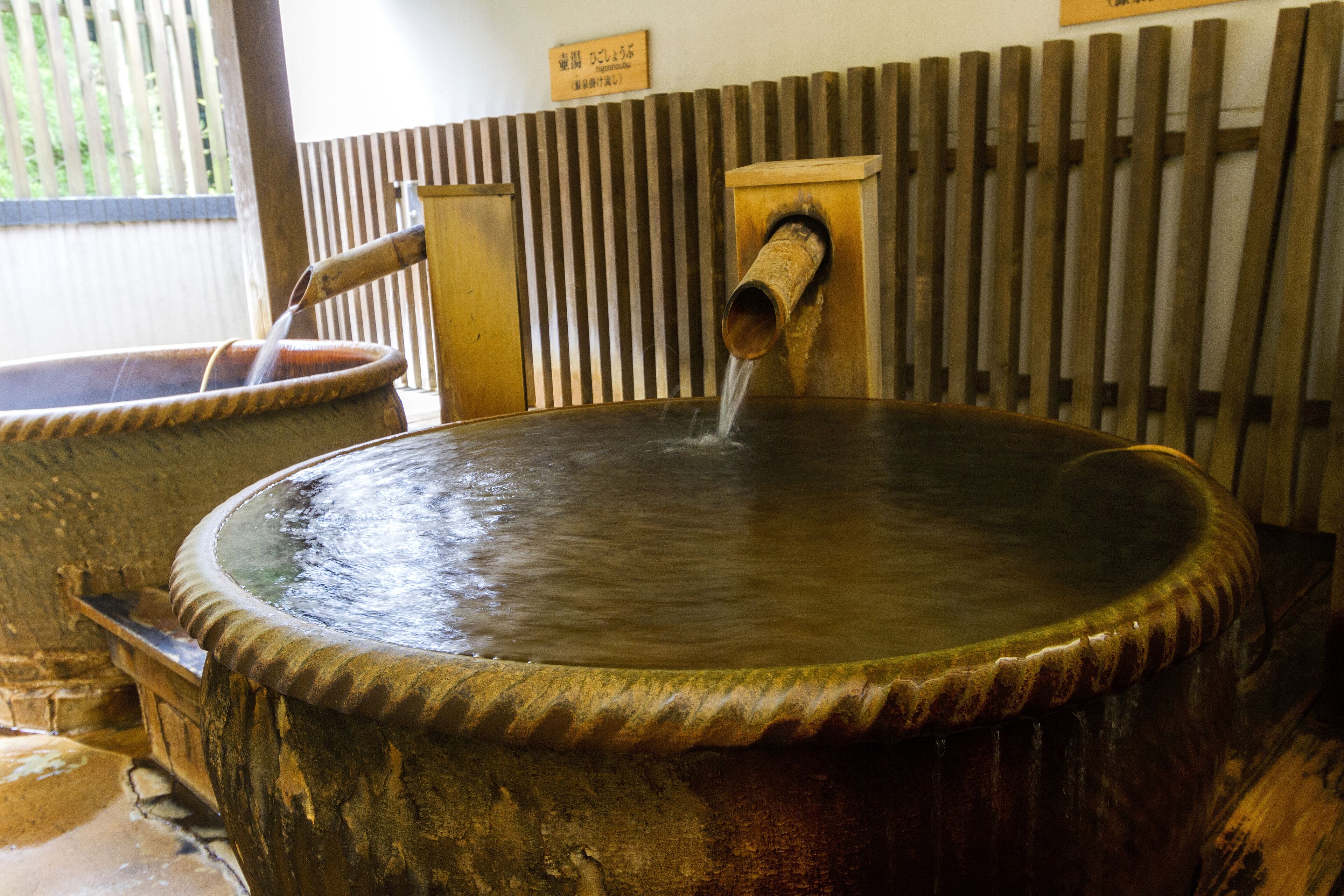 A traditional hot spring bath with a wooden structure and a metal spout.