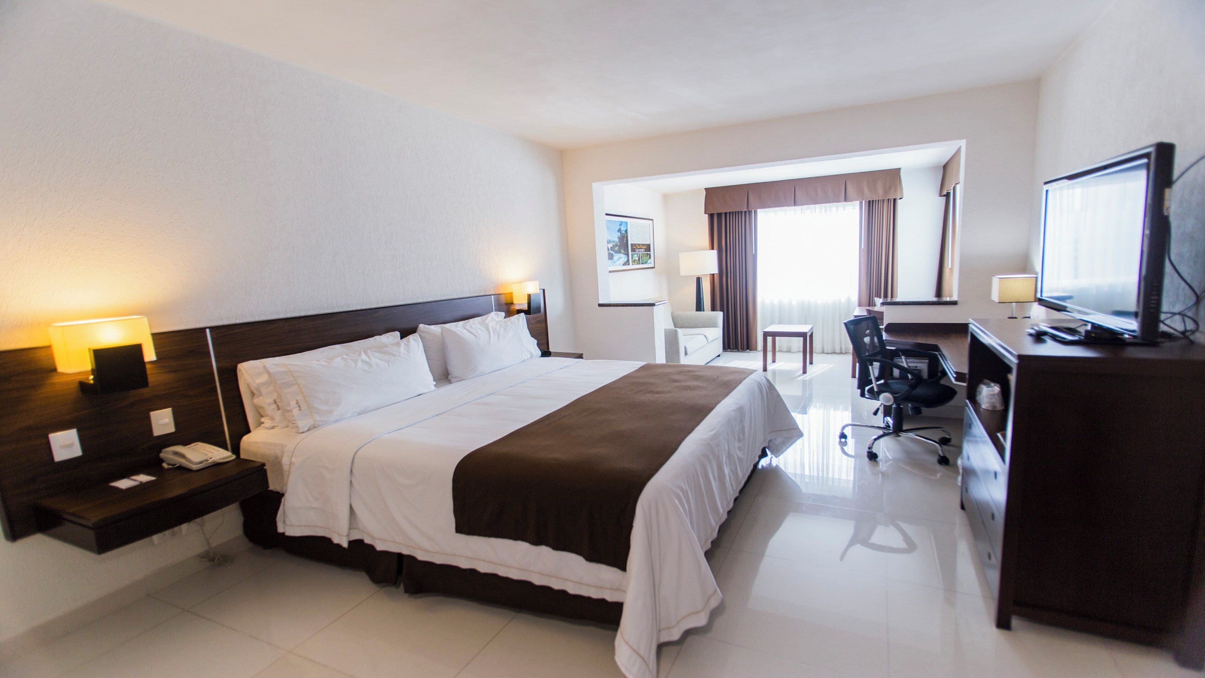 Una habitación de hotel con una cama grande, un escritorio con computadora, televisión y una silla.