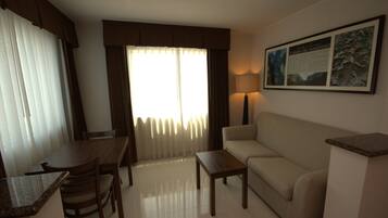 Habitación de hotel con mesa de comedor, sillas, sofá, lámpara y un cuadro en la pared.