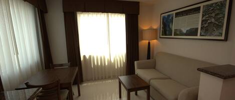 Habitación de hotel con mesa de comedor, sillas, sofá, lámpara y un cuadro en la pared.