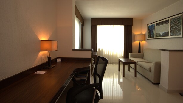 A hotel room with a wooden desk, a chair, a sofa, and a lamp. - Holiday Inn Express Tuxtla Gutierrez La Marimba by IHG (Tuxtla Gutierrez)