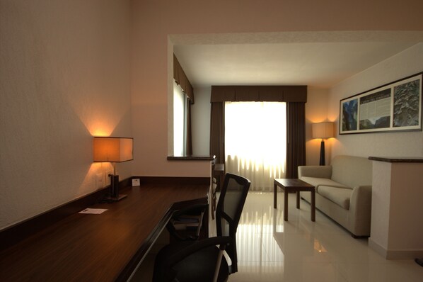 Een hotelkamer met een houten bureau, een stoel, een bank en een lamp.