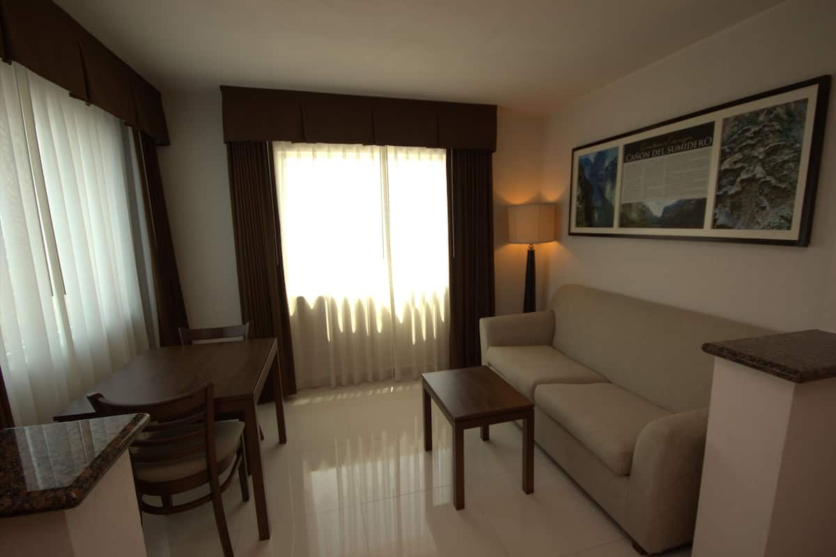 A hotel room with a dining table, chairs, a sofa, a coffee table, a lamp, and a framed picture on the wall.