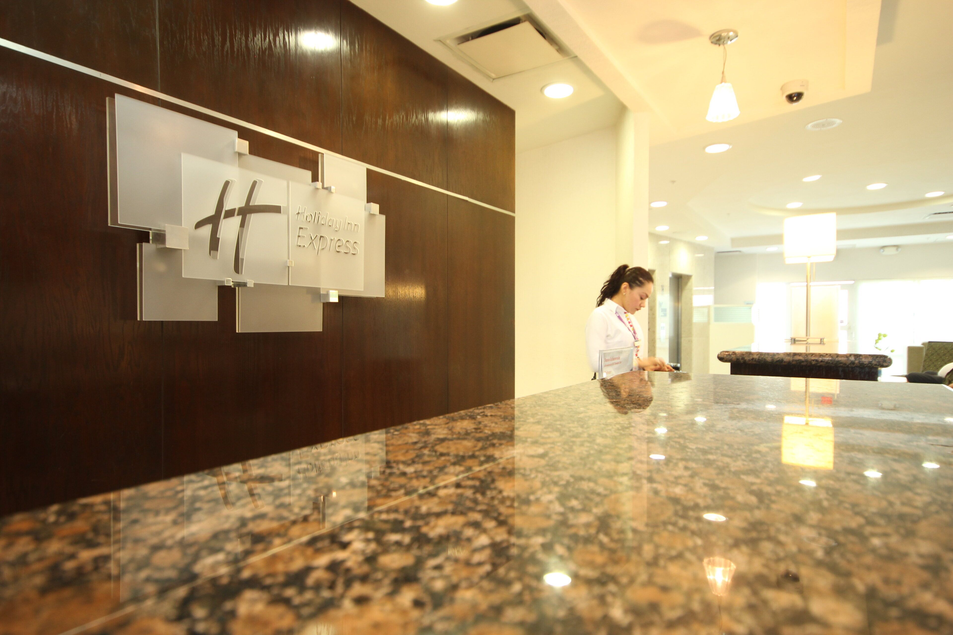 Una recepción con mostrador de mármol, una mujer de pie y un letrero que dice 'Holiday Inn Express'.