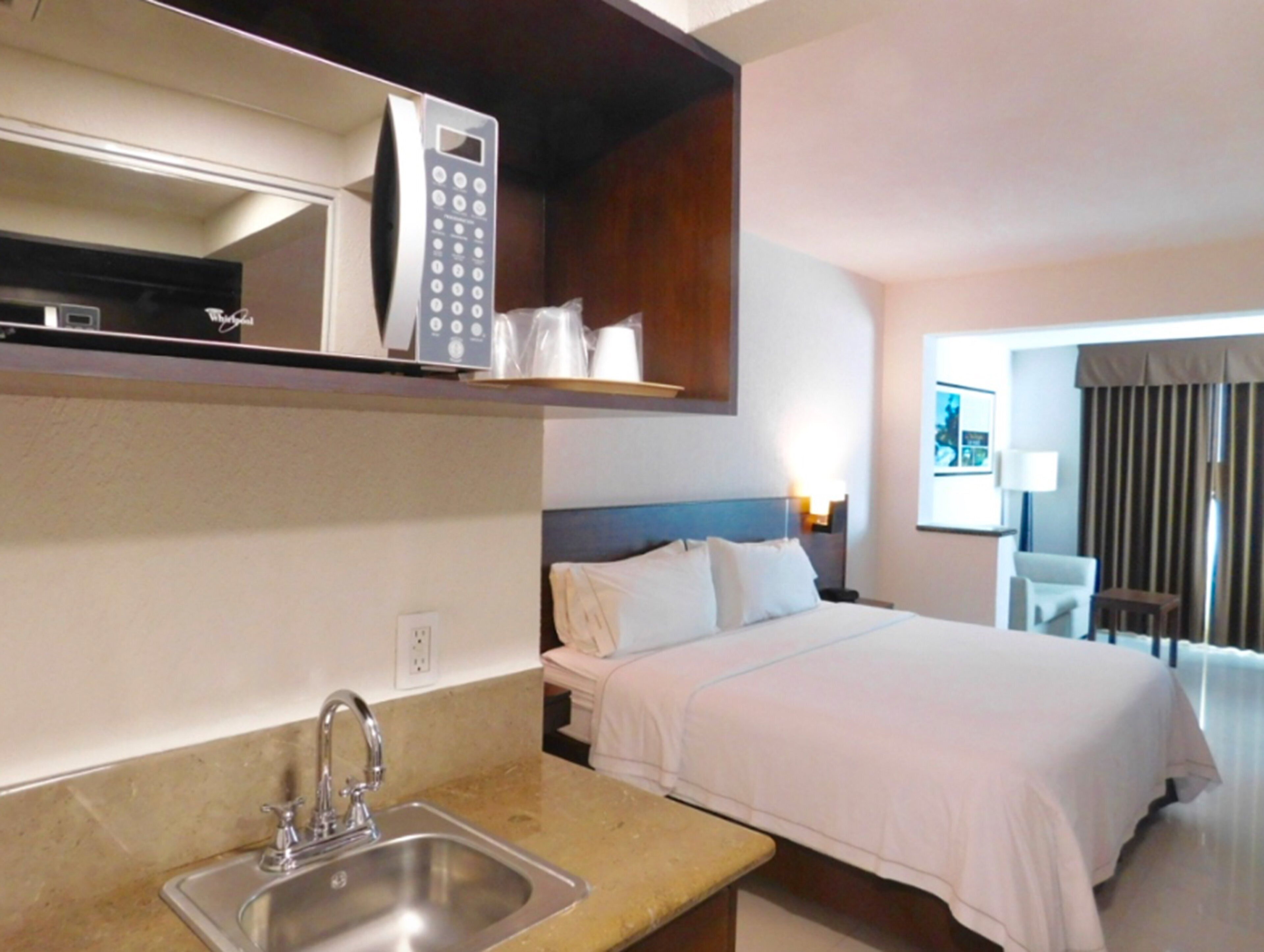 Habitación de hotel con cama, lavamanos, microondas y una silla.