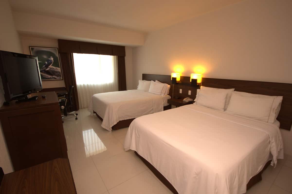 A hotel room with two beds, a desk with a television, and a window with curtains.
