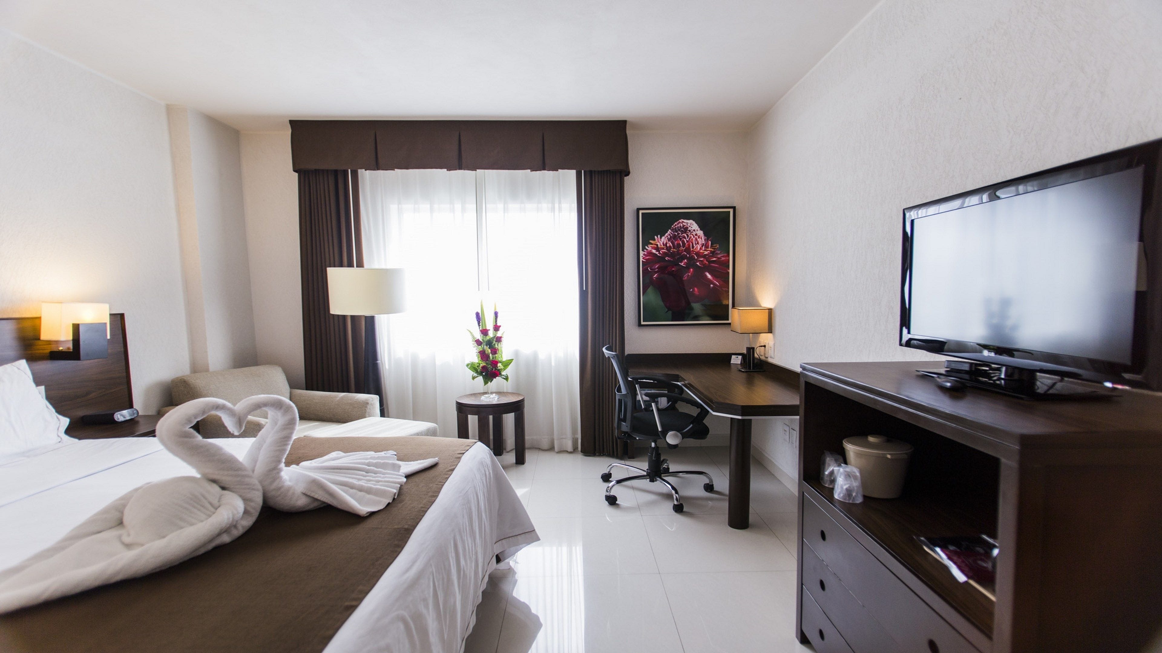 Een hotelkamer met een bed, een bureau, een stoel, een televisie en een schilderij aan de muur.