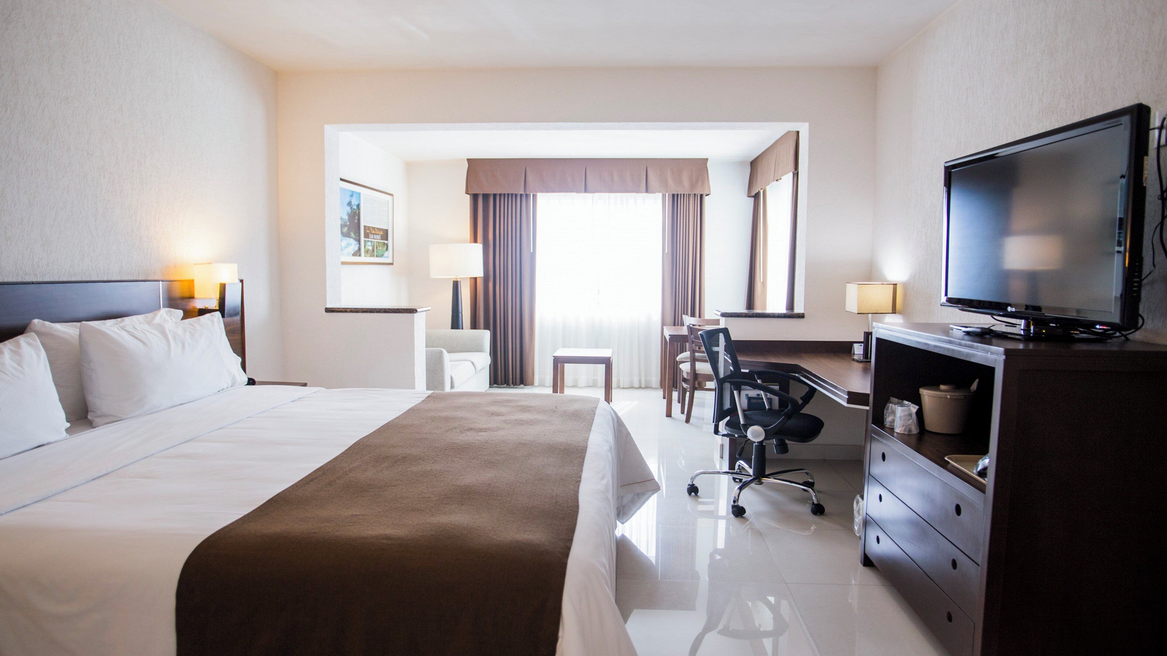 A hotel room with a large bed, a desk with a chair, a television, and a dresser.