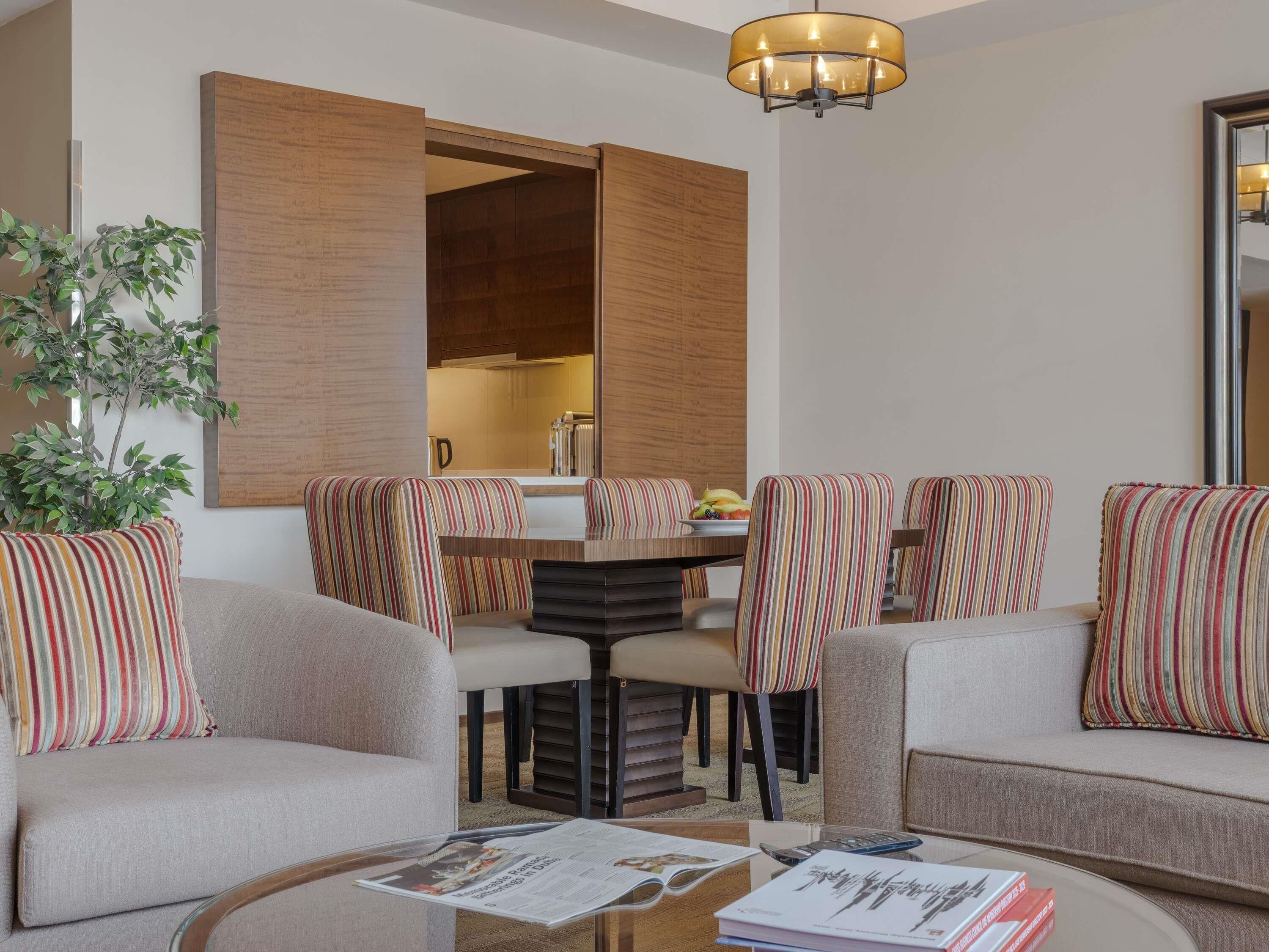 Een moderne woonkamer met een eethoek, met gestreept bekleden stoelen, een ronde salontafel en een grote houten kast.