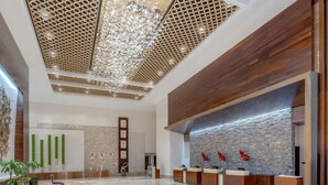 A modern lobby with a reception desk, a decorative ceiling, and a patterned floor.