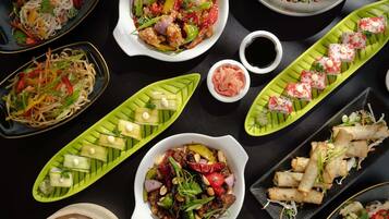 Diverse gerechten, zoals noedels, roerbakgroenten en sushi, op een zwarte tafel.