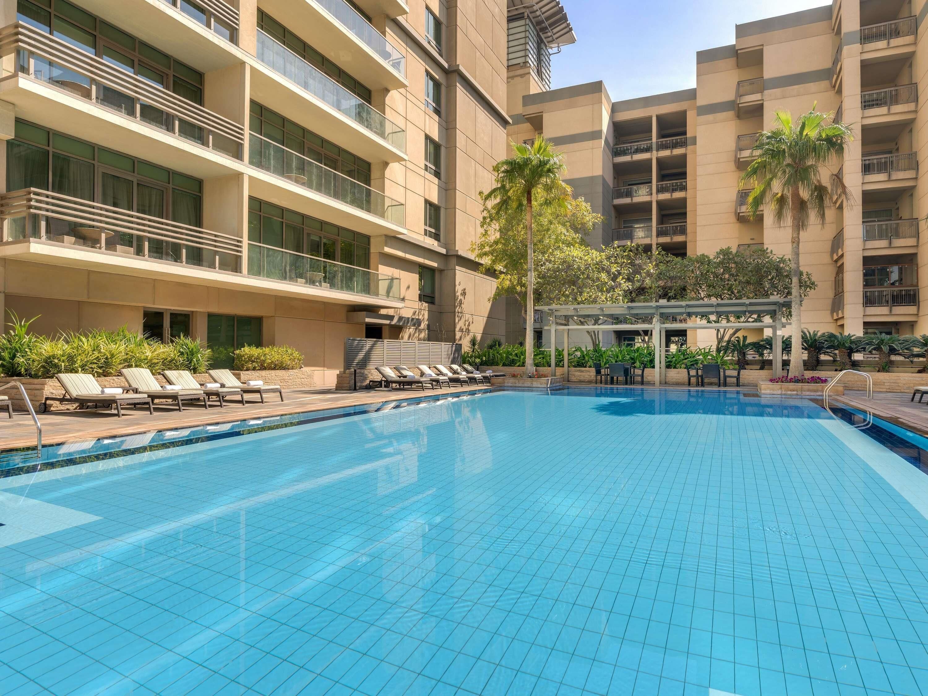 A swimming pool with lounge chairs, a pergola, and a palm tree.