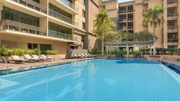 A swimming pool with lounge chairs, a pergola, and a palm tree.
