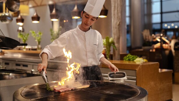 A chef cooking with flames on a grill in a modern kitchen setting.
