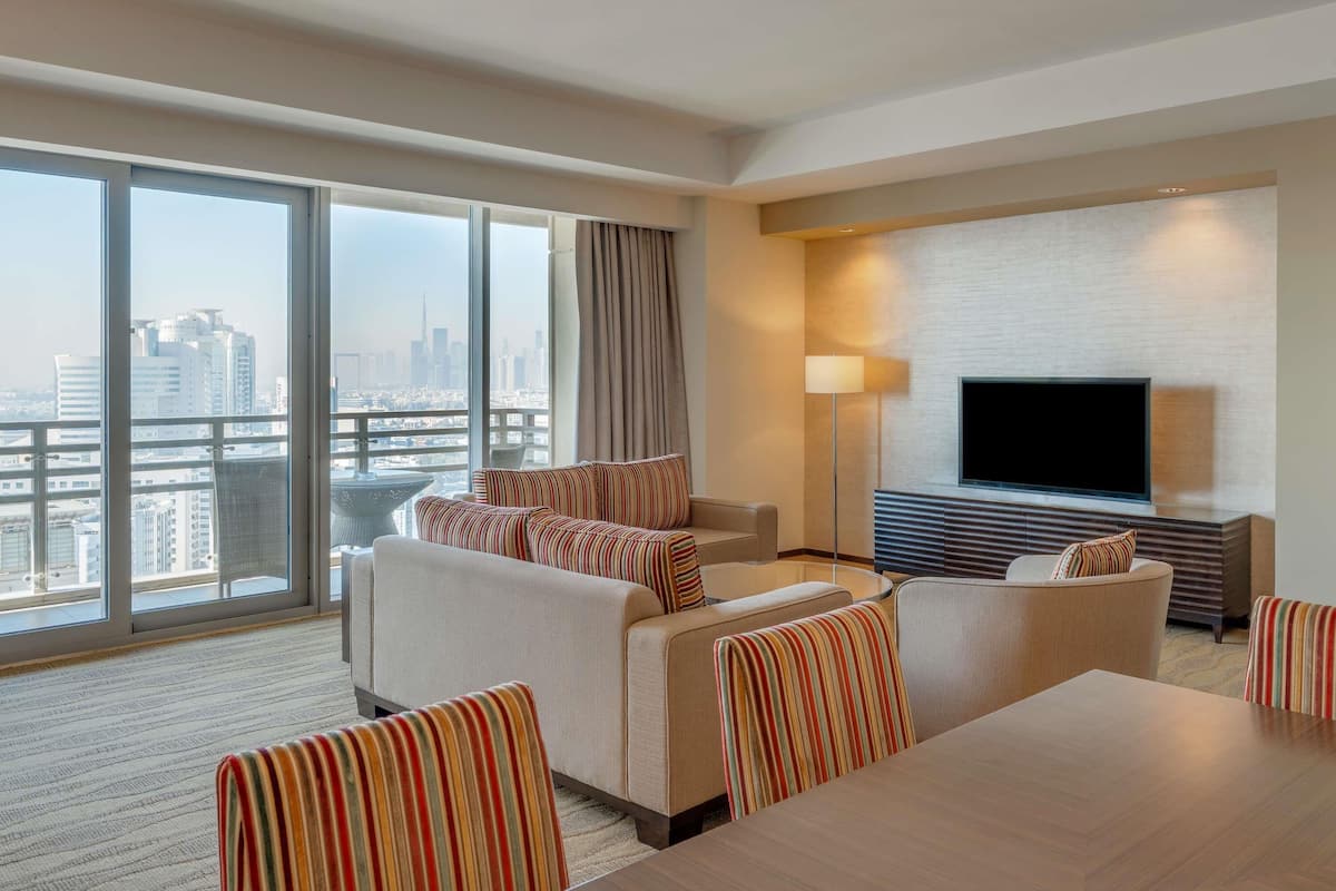 A hotel room with a large window, a sofa set, a TV, and a lamp.