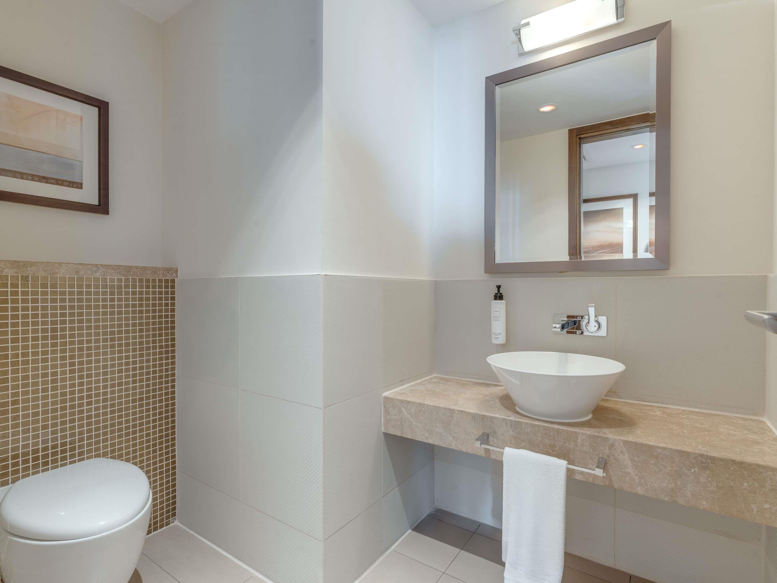 Un baño con inodoro, lavabo con espejo y toalla en un perchero.