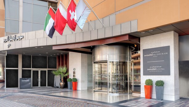 A hotel entrance with flags, a revolving door, and potted plants.
