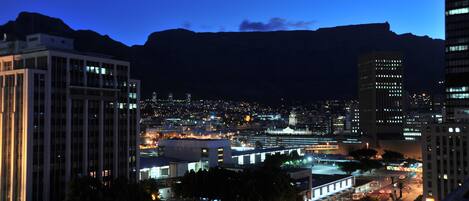A cityscape at dusk with illuminated buildings and a mountain in the background.