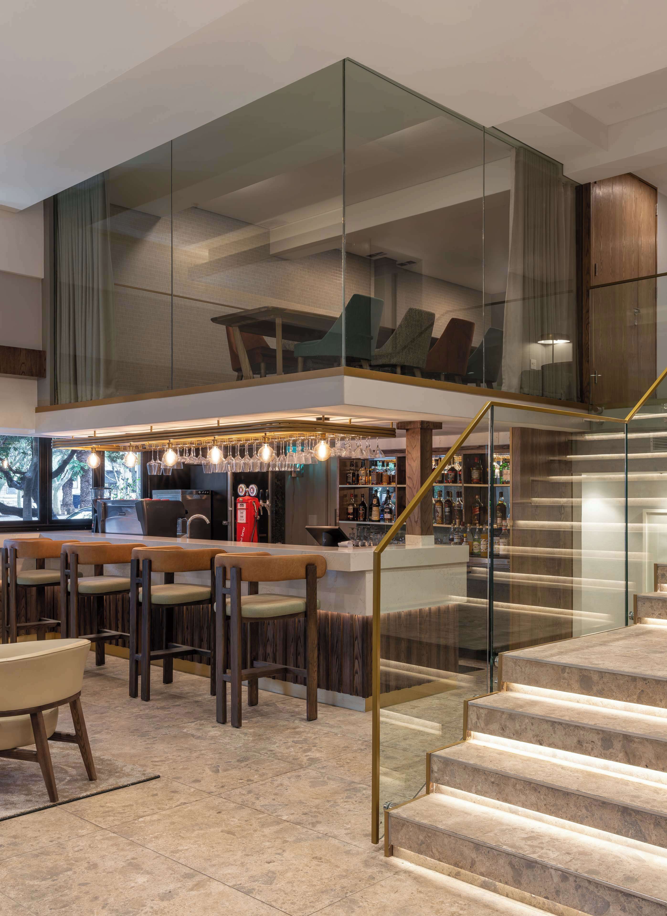 Un área de bar moderna con asientos, una escalera y barandilla de vidrio.