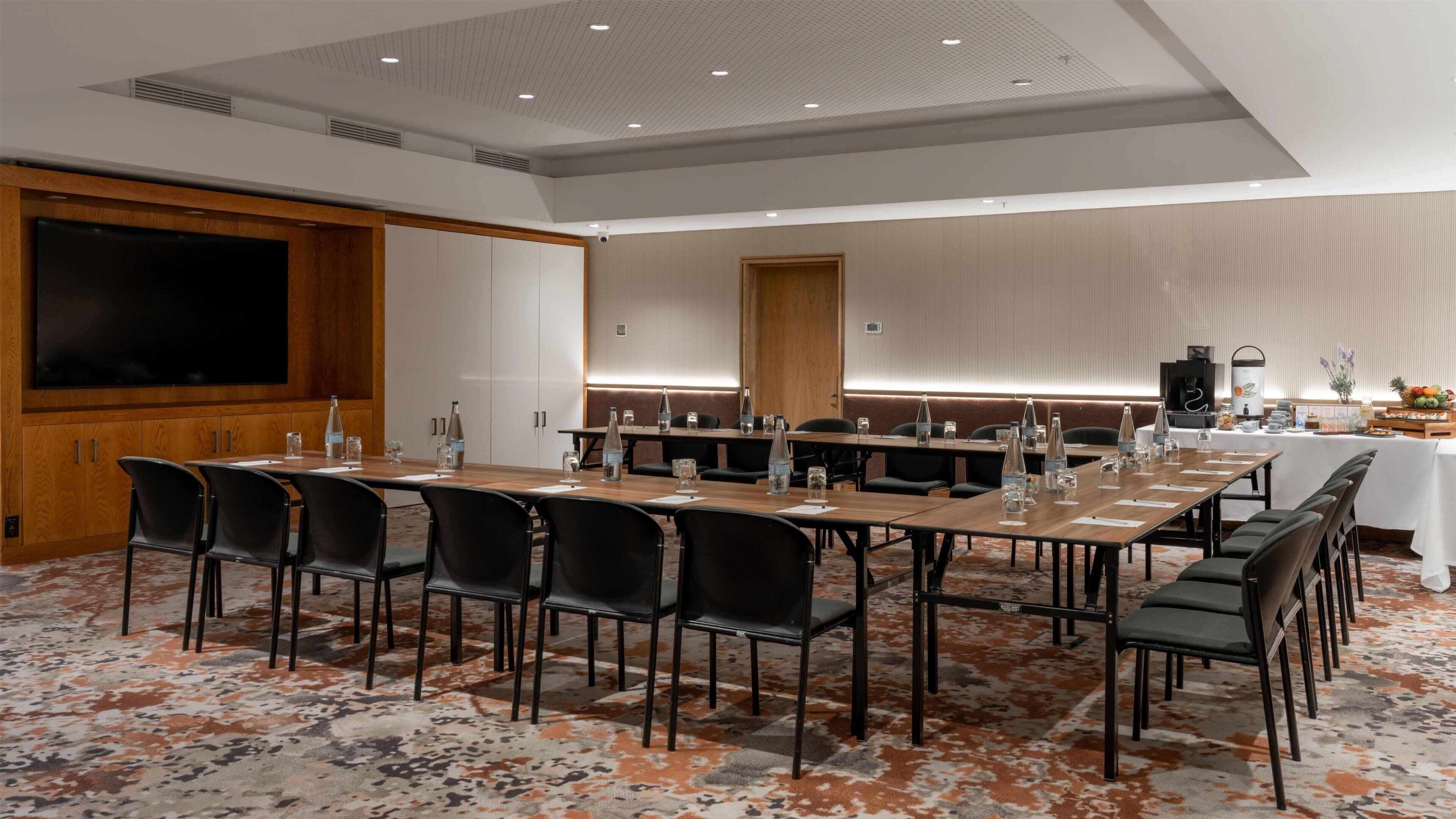 A conference room with a long table, chairs, and a large screen.