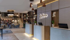 A modern reception area with a bar, seating, and a reception desk with a 'Radisson' sign. - Radisson Hotel Cape Town Foreshore (Cape Town)