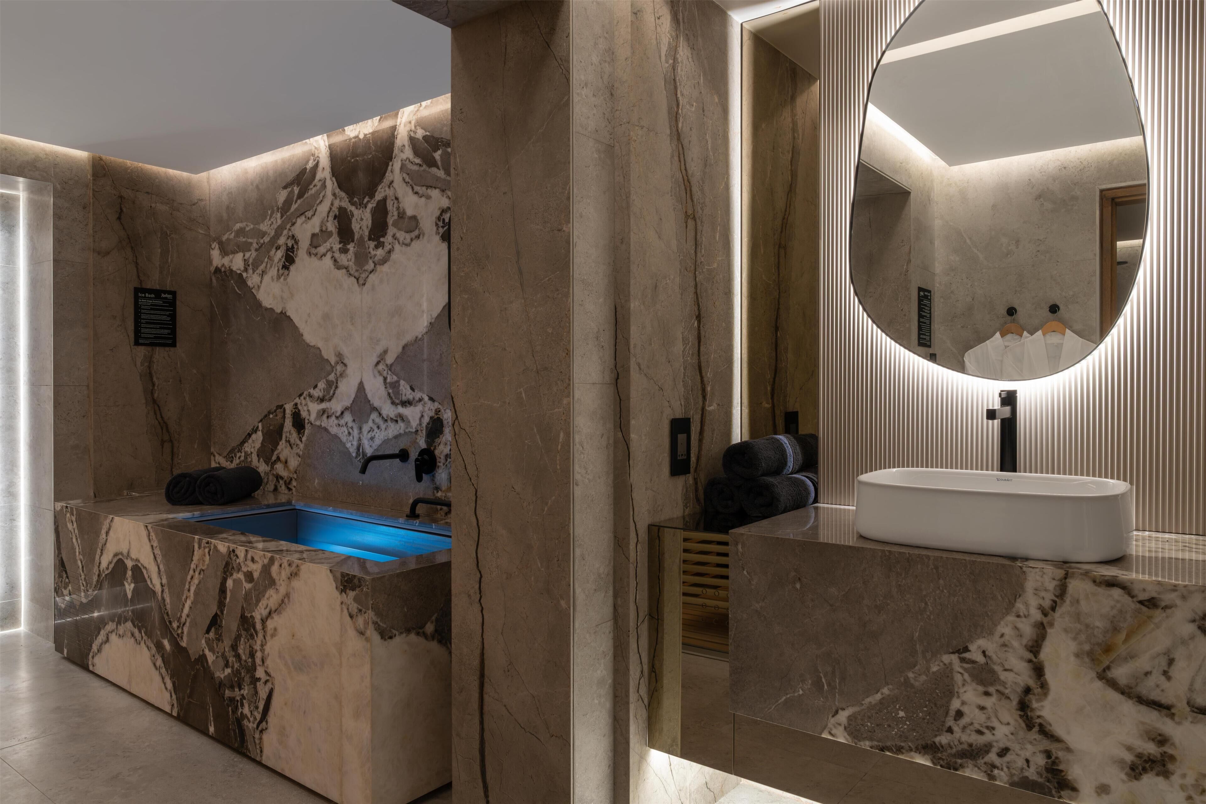 A modern bathroom with a marble sink, a built-in bathtub, and a large mirror.