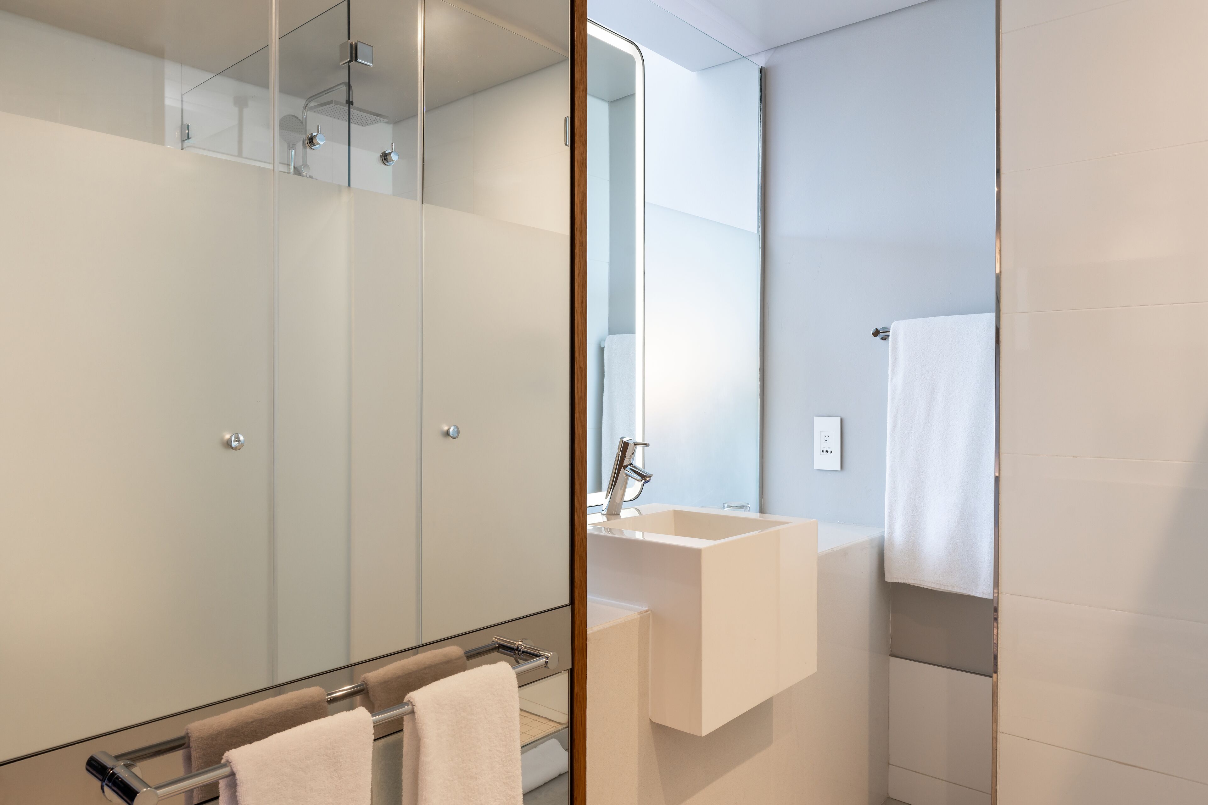 A modern bathroom with a glass shower enclosure, a white sink, and a mirror.