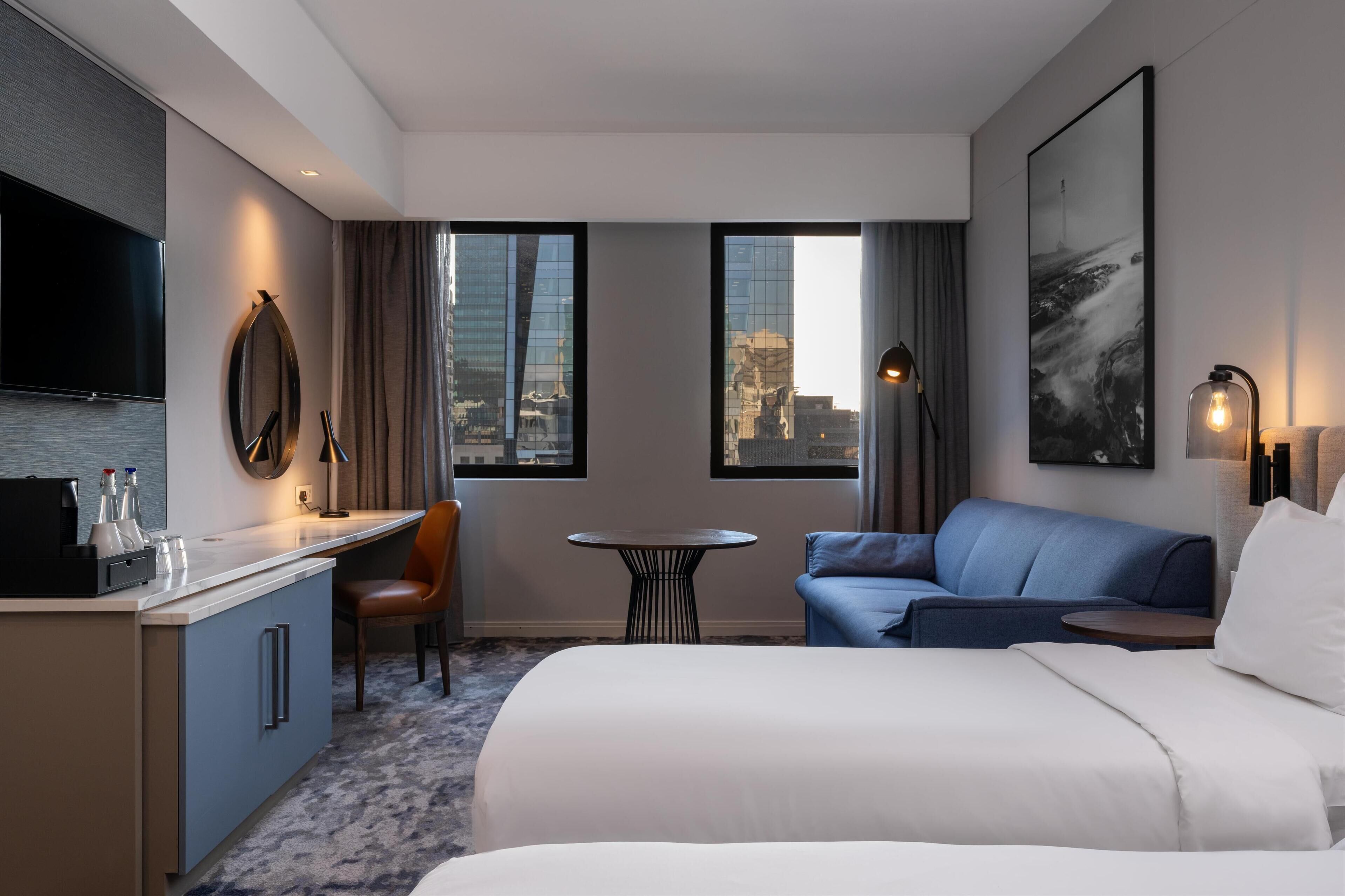 Quarto de hotel com cama, escrivaninha, cadeira, mesinha e sofá.