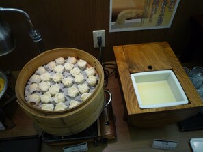 A steam cooker with dumplings, a wooden table, and a white basin. - Route Inn Grantia Komatsu Airport (Komatsu)