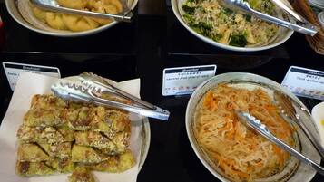 Buffet com diversos pratos, incluindo tempura, uma salada e um prato de macarrão.