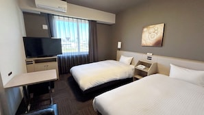 Ein Hotelzimmer mit zwei Betten, einem Fernseher, einem Schreibtisch und einem Fenster mit Vorhängen.